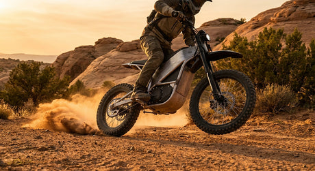 An electric dirt bike tearing through a dusty off-road trail at golden hour, surrounded by rugged rocky terrain.
